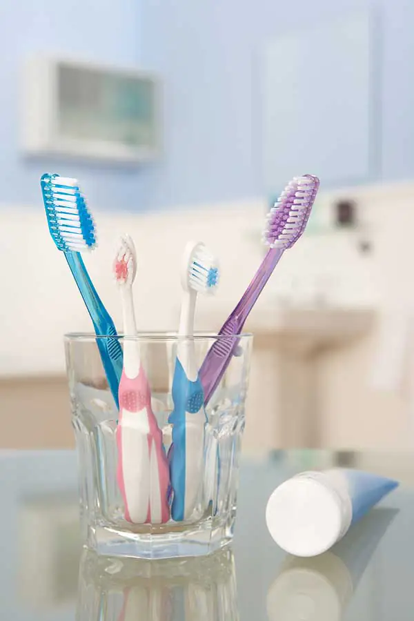 A cup with 2 large toothbrushes and 2 smaller toothbrushes, with a tube of toothpaste beside the cup.